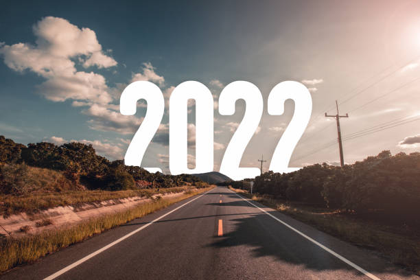 The word 2022 behind the tree of empty asphalt road at golden sunset and beautiful blue sky. stock photo