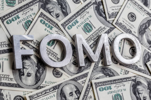 The word FOMO laid with aluminium letters on the US dollar banknotes background - with selective focus The word FOMO - fear of missing out - laid with aluminium letters on the US dollar banknotes background - with selective focus. fomo photos stock pictures, royalty-free photos & images