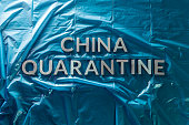 the words china quarantine laid with brushed silver metal letters on crumpled blue plastic film in flat lay straight perspective and dramatic light