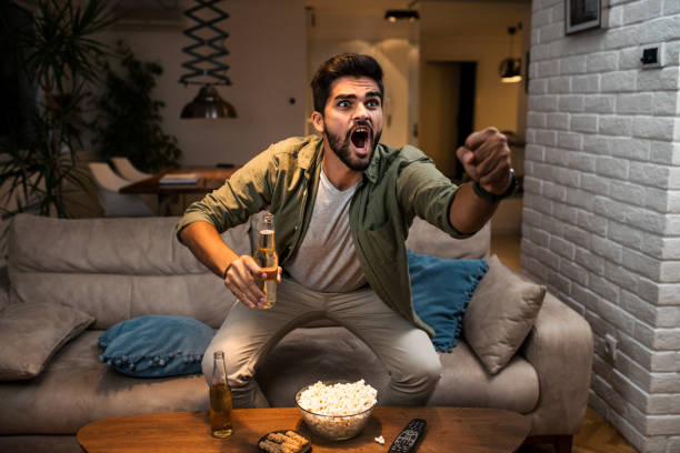 The young man is watching a sports game on TV The young man is watching a sports game on TV fan enthusiast stock pictures, royalty-free photos & images