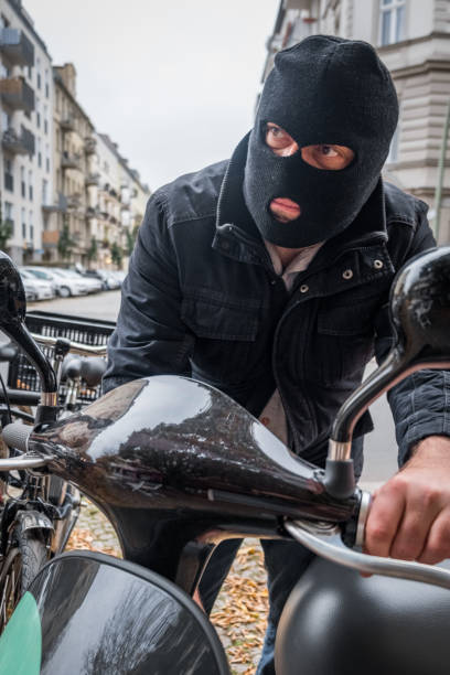 Theft wearing a balaclava stealing a scooter Theft wearing a balaclava stealing a scooter ski mask criminal stock pictures, royalty-free photos & images
