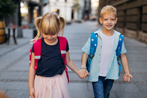 Young blond girl holding her brothers hand while walking to school