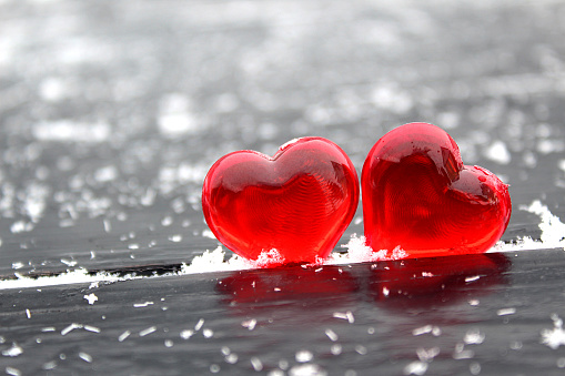 Theme for Valentine's Day. Two red hearts stand on a black background with snowflakes.