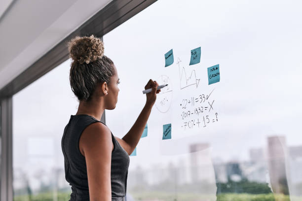 There's a new plan on the wall Shot of a young businesswoman writing on a glass wall in an office business goals stock pictures, royalty-free photos & images