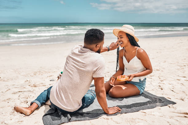 There's nothing more romantic than a picnic on the beach Shot of a young couple having a picnic together at the beach couple eating chocolate stock pictures, royalty-free photos & images