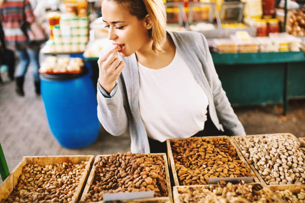 These almonds are delicious. Beautiful blonde woman tasting almonds  at food market. chestnut food stock pictures, royalty-free photos & images