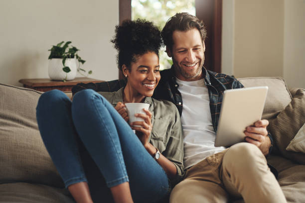 These apps make sure we always stay entertained Shot of a happy young couple using a digital tablet together while relaxing on a couch at home sofa stock pictures, royalty-free photos & images