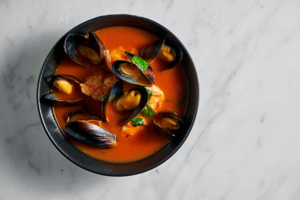 Thick Tuscan caciucco soup with seafood. Classic red soup with mussels, scallops and fish in a black plate on a marble background. stock photo