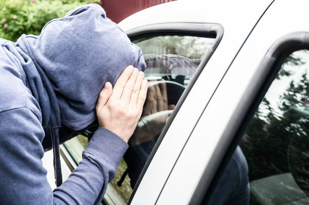 A thief in a jacket with a hood looks into the car through a closed window. stock photo