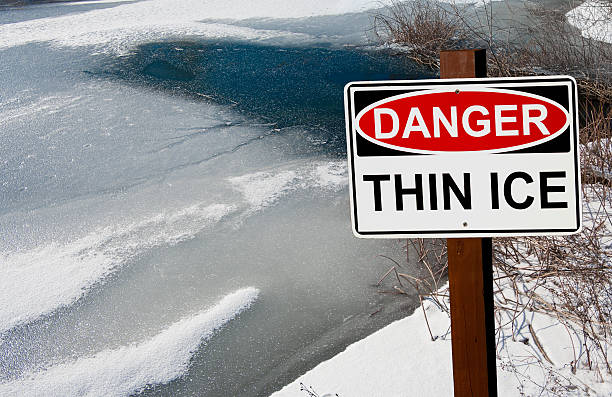 Thin Ice Warning Sign A sign warns of danger as ice thaws on a pond in southern Wisconsin. thin stock pictures, royalty-free photos & images
