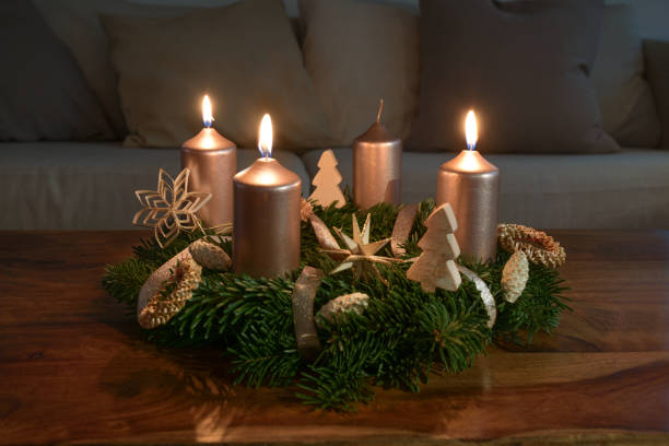 Third Advent with three lit golden candles on an Advent wreath with natural Christmas decoration on a wooden coffee table, copy space, selected focus stock photo