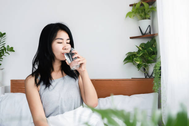 thirsty Asian woman drinking water in bed after wake up stock photo