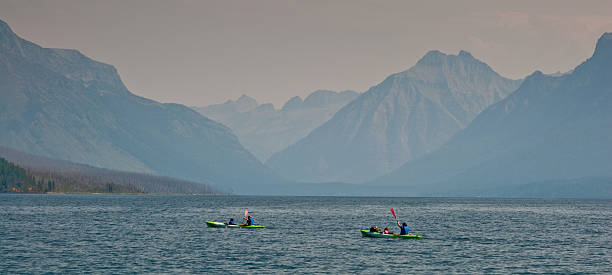 Kayakers on Lake McDonald Glacier National Park, Montana, USA - August 12, 2013: This family in two kayaks is paddling across Lake McDonald on a hazy day. jeff goulden panoramic stock pictures, royalty-free photos & images