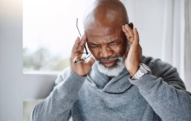 This headache is unbearable! Shot of a handsome senior man suffering with a headache at home headache stock pictures, royalty-free photos & images