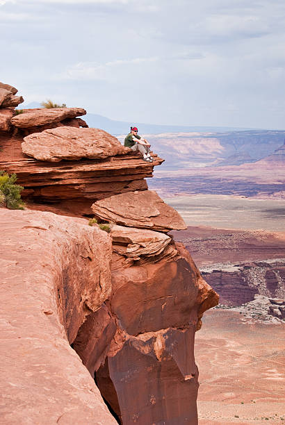 Living Life on the Edge Canyonlands National Park, Utah, USA - May 17, 2012: This hiker is sitting on a precarious rock outcrop at Grandview Overlook and looking into the canyon. jeff goulden canyonlands national park stock pictures, royalty-free photos & images