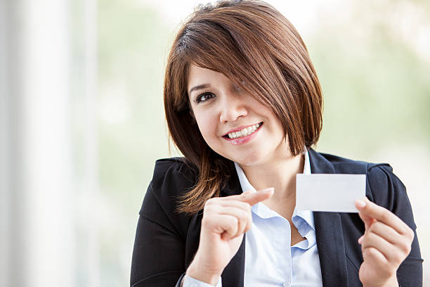Happy young businesswoman holding a business card in one hand and...