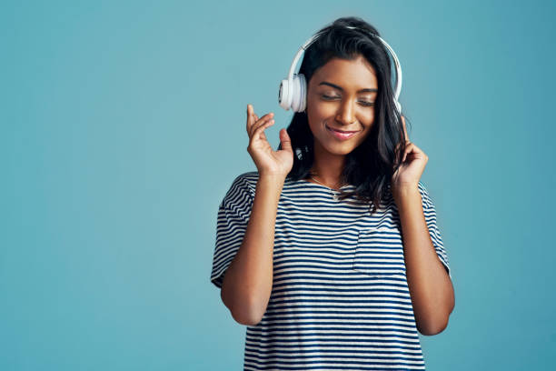 This is my kinda music! Cropped shot of a beautiful young woman wearing headphones against a blue background listening stock pictures, royalty-free photos & images