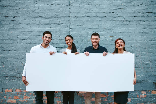 This is something worth taking note of Portrait of a group of businesspeople holding a blank placard against a grey wall outside banner sign stock pictures, royalty-free photos & images