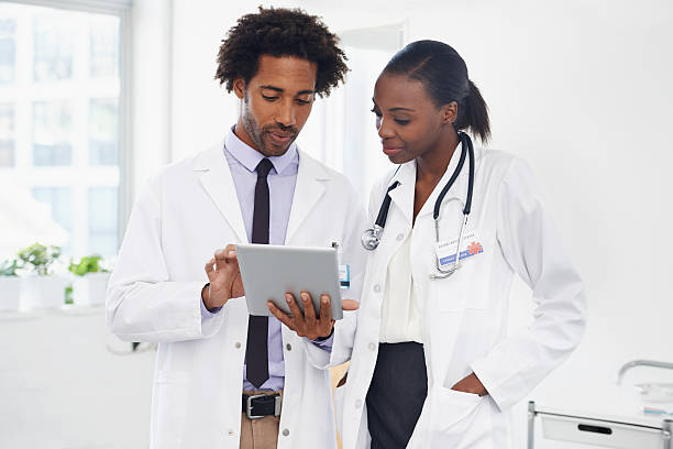 This is the correct diagnosis Shot of two doctors standing in a room using a digital tablet physician assistant stock pictures, royalty-free photos & images