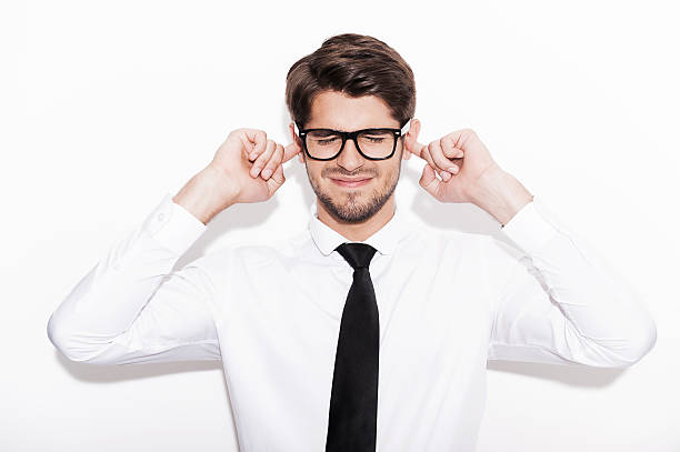 This is too loud! Frustrated young man holding fingers in ears and keeping eyes closed while standing against white background Fingers in Ears stock pictures, royalty-free photos & images