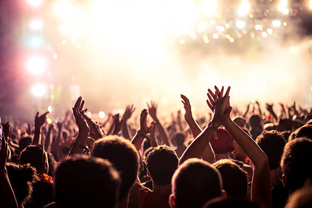 This party's on fire Audience with hands raised at a music festival and lights streaming down from above the stage. Soft focus, blurred movement. cheering stock pictures, royalty-free photos & images