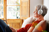 Shot of a mature woman sitting on her sofa listening to music on a digital tablet