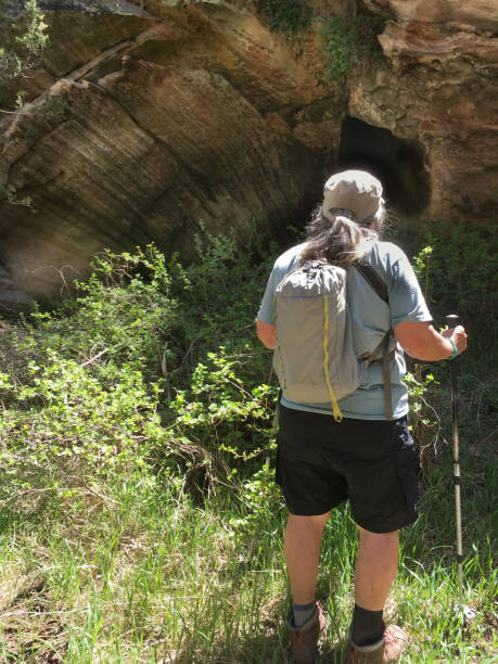 Woman Hiker Looking into a Cave This woman hiker is examining a cave opening near Fisher Point. Fisher Point is on the Walnut Canyon Trail in the Coconino National Forest near Flagstaff, Arizona, USA. jeff goulden people stock pictures, royalty-free photos & images