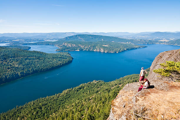 Couple Sitting on a Rock Ledge Saltspring Island, British Columbia, Canada - September 06, 2012: This young couple are playing music and enjoying the view from a ledge on Mount Maxwell in Mount Maxwell Provincial Park. jeff goulden seascape stock pictures, royalty-free photos & images