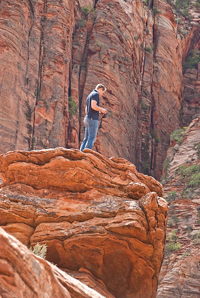 Young Man Taking Picture from a Rock Formation Zion National Park, Utah, USA - May 11, 2011: This young hiker is taking a picture from the Canyon Overlook trail. jeff goulden zion national park stock pictures, royalty-free photos & images