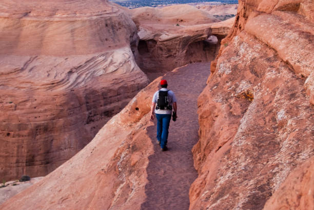 Hiking the Delicate Arch Ledge Trail Arches National Park, Utah, USA - May 16, 2012: This young man is hiking the narrow trail to Delicate Arch in the evening. jeff goulden mojave desert stock pictures, royalty-free photos & images