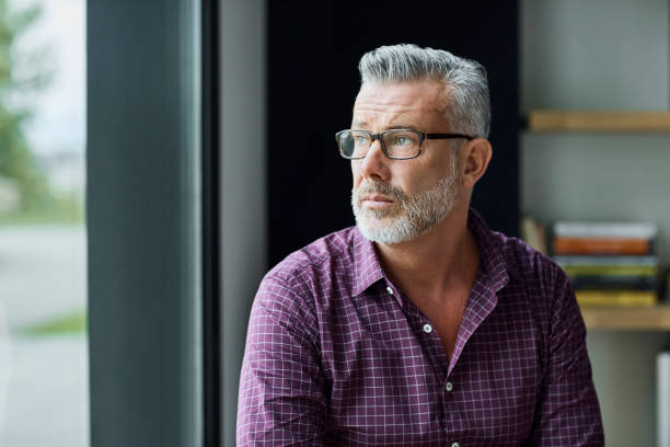 Thoughtful businessman looking away in office Thoughtful businessman looking away in office. Senior executive is wearing shirt at workplace. He is looking through window. looking away stock pictures, royalty-free photos & images