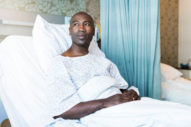 Thoughtful patient lying on bed in hospital Thoughtful patient lying on bed. Mid adult man is wearing hospital gown. He is looking away. 35 39 years photos stock pictures, royalty-free photos & images