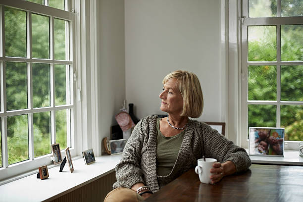 Thoughtful senior woman having coffee Thoughtful senior woman having coffee at table in cottage introspection stock pictures, royalty-free photos & images