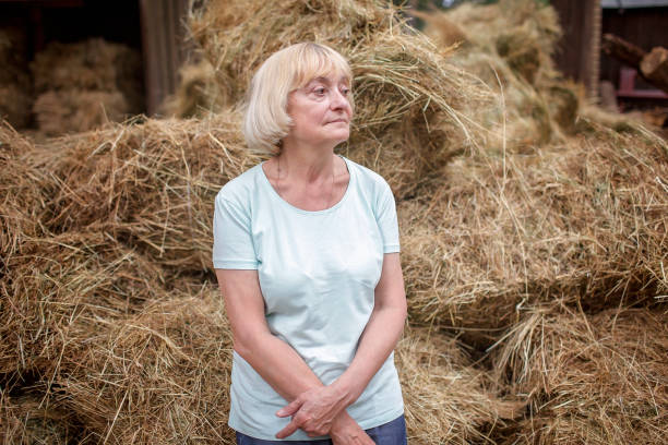 Thoughtful senior woman staying near haystack on farm, escape to be in calm and harmony stock photo