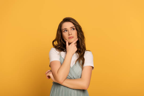 thoughtful spring woman with long hair isolated on yellow thoughtful spring woman with long hair isolated on yellow hand on chin stock pictures, royalty-free photos & images