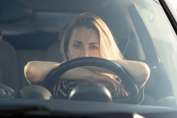 Thoughtful tired woman driving car, looking through windshield at camera, thinking about something. stock photo