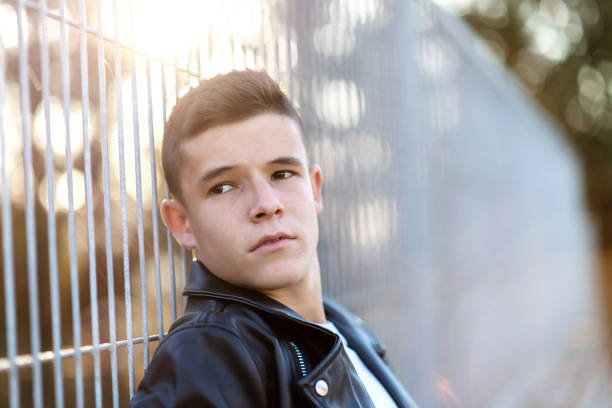 Thoughtful young man leaning on chain link fence stock photo