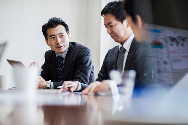 Three businessmen meeting in a conference room. Man in the back has a digital tablet japanese ethnicity stock pictures, royalty-free photos & images