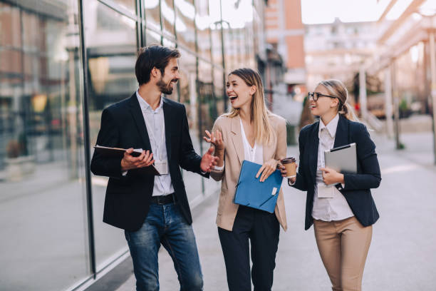 Three cheerful young business people talking to each other while walking outdoors stock photo