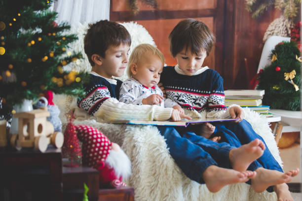 Three children, boy brothers, sitting in rocking chair in cozy living room with christmas decoration, reading a book Three children, boy brothers, sitting in rocking chair in cozy living room with christmas decoration, reading a book, smiling christmas story telling stock pictures, royalty-free photos & images