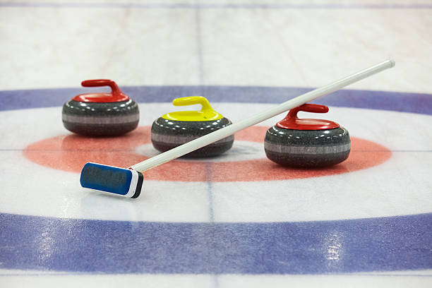 three curling rocks and a sweeper on ice rink  - curling stockfoto's en -beelden
