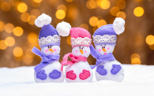 Three cute snowmans made of felt. Beautiful golden bokeh lights on the background stock photo