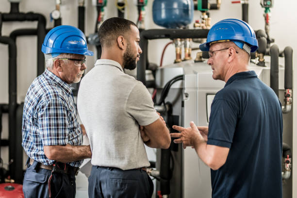 Three engineers talking next to a boiler Three engineers standing next to a boiler in a house and talking. african american plumber stock pictures, royalty-free photos & images