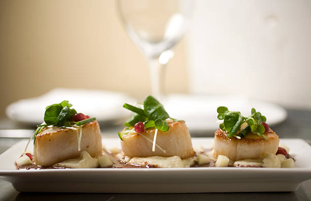 Three fancy scallops on a plate with parsley and sauce stock photo