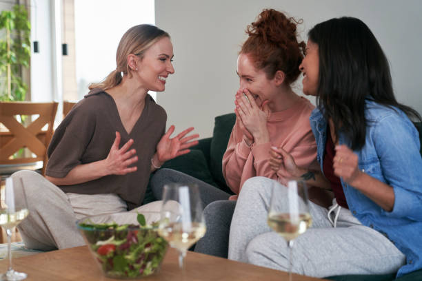 Three  female caucasian friends chatting and drinking wine at home stock photo