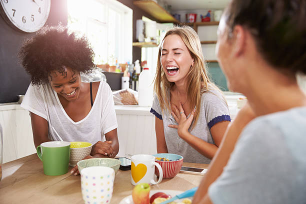 Three female friends laughing at breakfast Three Female Friends Enjoying Breakfast At Home Together roommate stock pictures, royalty-free photos & images