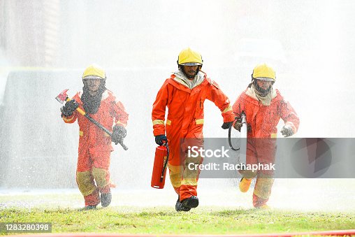 istock Three firefighters in uniform walking forward holding a fire extinguish tools surround with water drops and spray. 1283280398