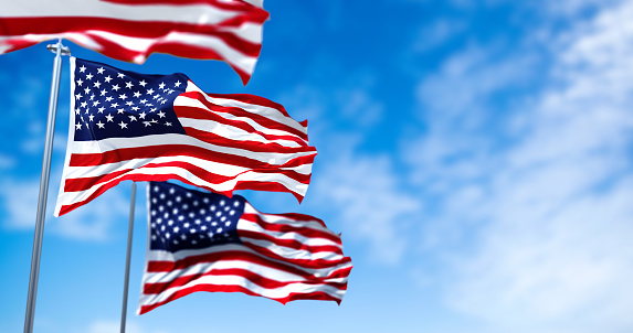 Three flags of the United States of America waving in the wind. Clear sky in the background. Selective focus. Democracy, independence and election day. Patriotic symbol of American pride