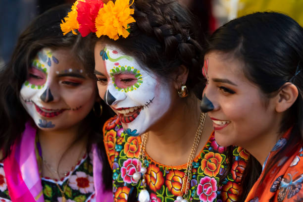 Oaxaca City, Oaxaca, Mexico– October 31, 2018:  Three friends in costume and makeup in the zócalo (city square) for the Día de los Muertos festival.  This annual holiday is celebrated extensively in southern Mexico with face painting, costumes, parades, dancing, altars, and graveside vigils. Celebration of the Día de los Muertos has been adopted in many other parts of the world.