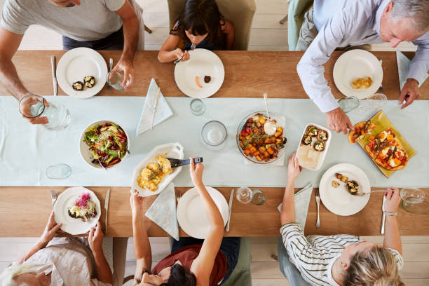 Three generation white family sitting at a dinner table together serving a meal, overhead view  dining table stock pictures, royalty-free photos & images